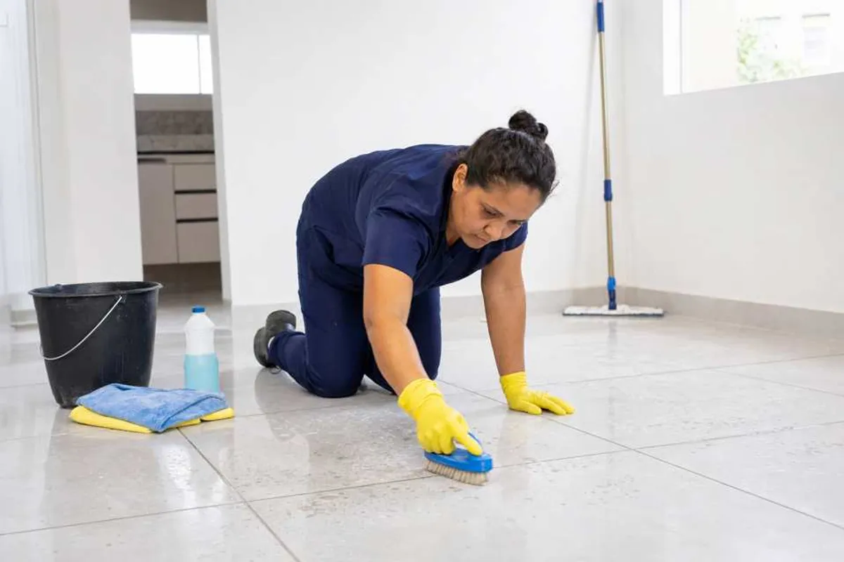 Profissional de limpeza pós obra residencial limpando rejunte e removendo poeira de cimento em imóvel reformado na Bela Vista